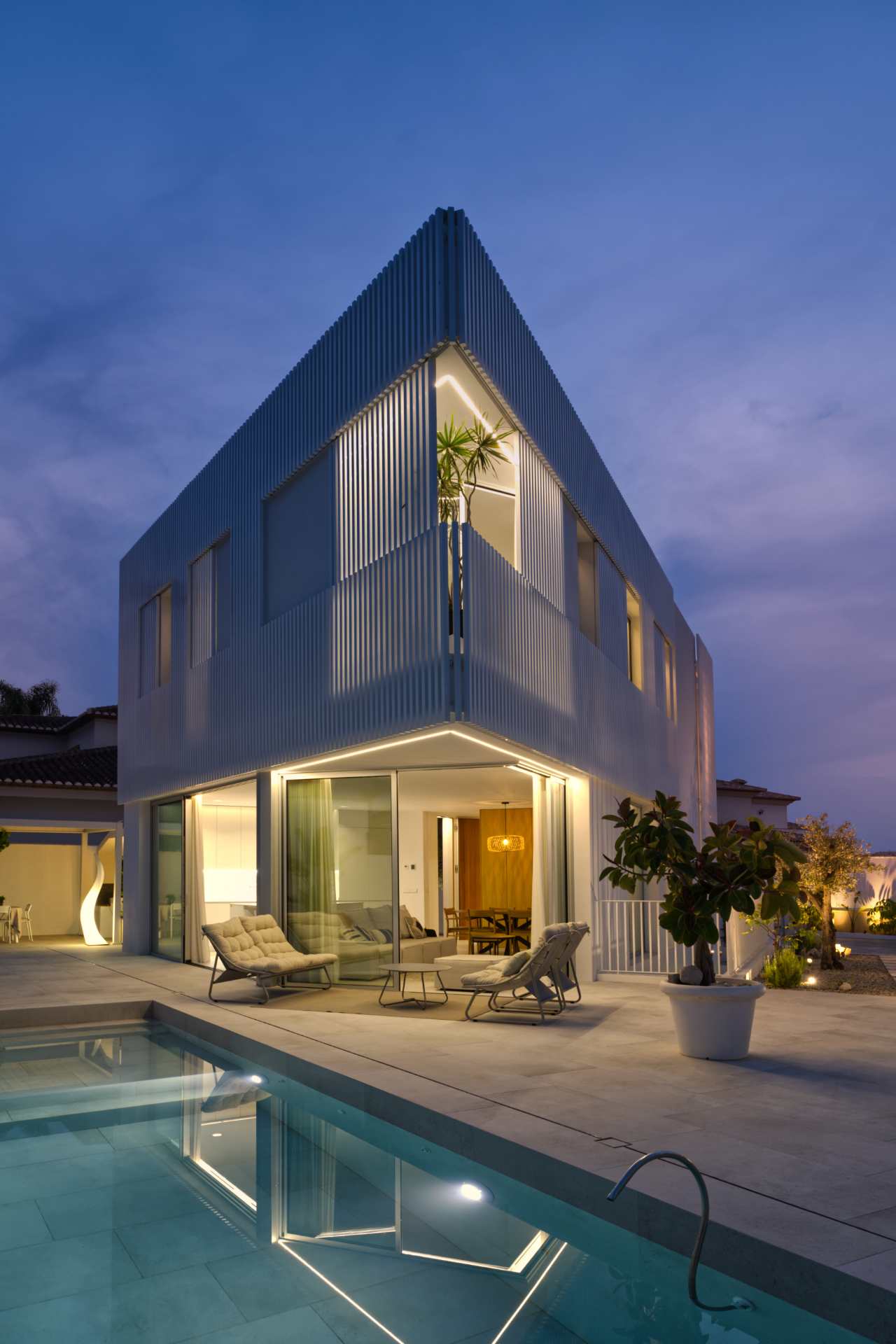 Casa moderna blanca con piscina iluminada al anochecer Fotografía de una casa moderna blanca al atardecer con piscina y diseño minimalista en España